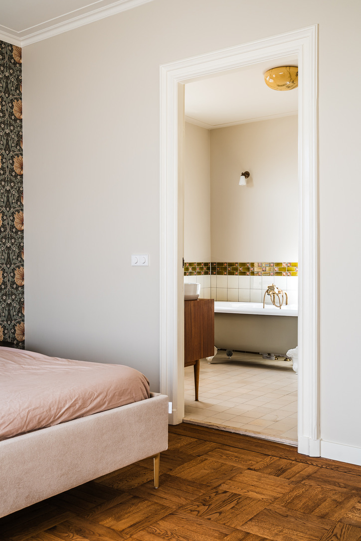 Doorkijk vanuit de slaapkamer naar de badkamer met historische tegelrand en vrijstaand bad op pootjes